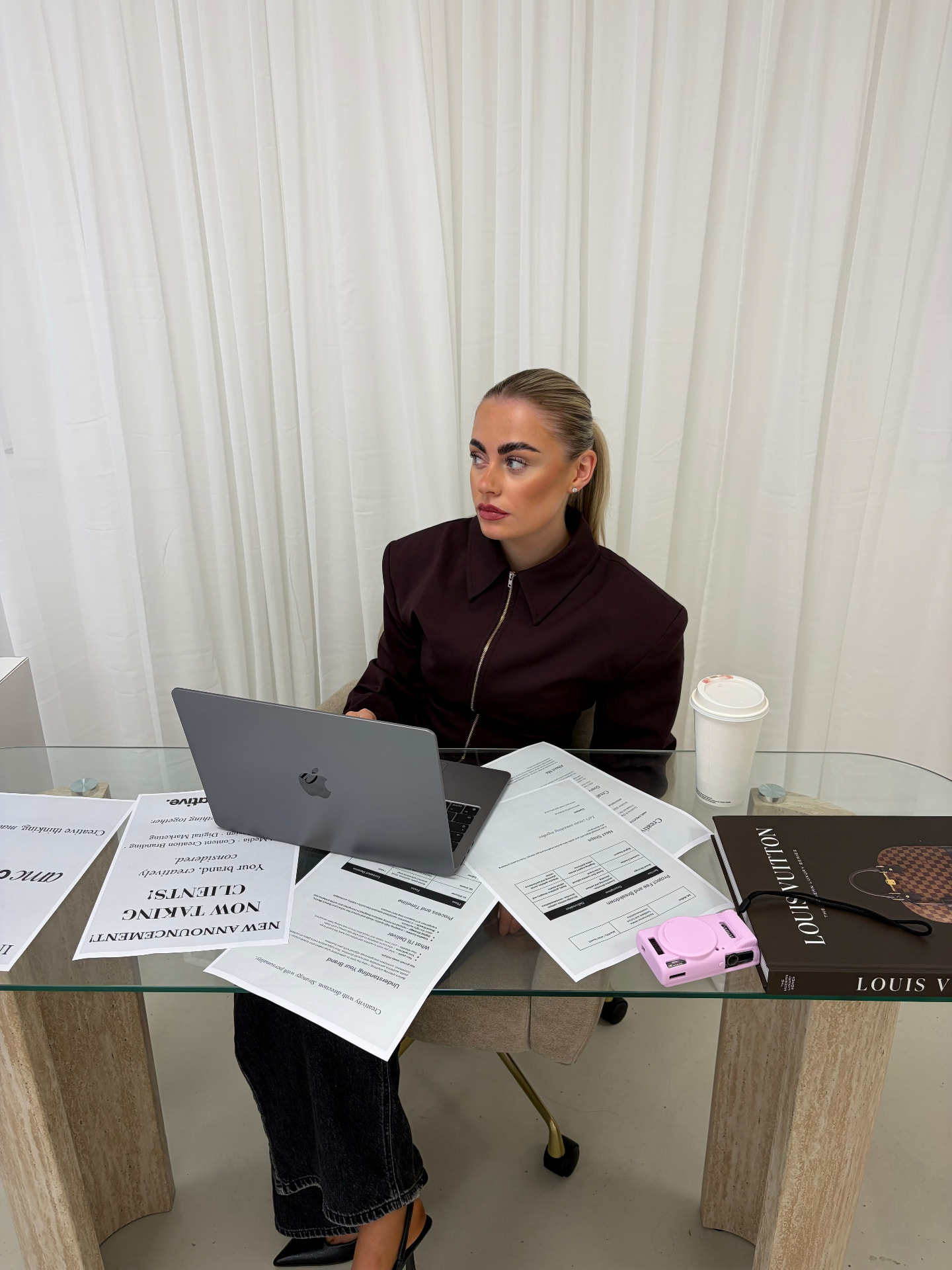 Seated at a glass desk covered with project documents